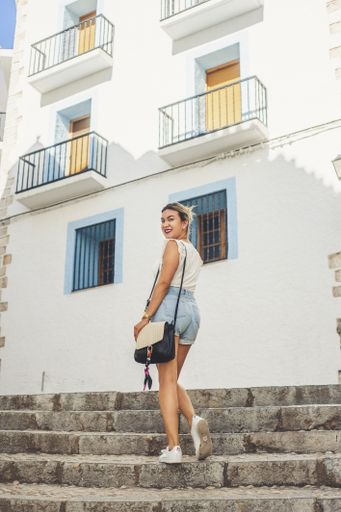 A vertical shot of a young Hispanic female wearing shorts and posing on the steps of a residential building