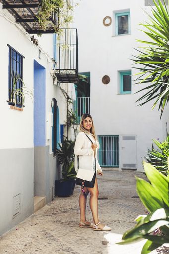 A vertical shot of a young Hispanic female posing on an alley surrounded by buildings under the sunlight