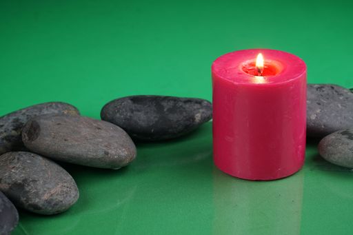 A red burning candle next to rocks with on a green surface