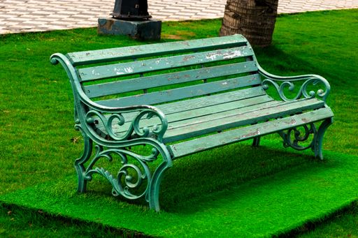 A wooden old green bench surrounded by green grass in a park