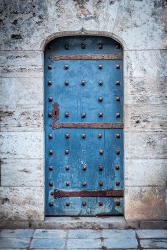 A vertical shot of a rusty blue door on a wooden exterior wall