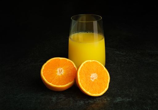 The glass of orange juice with half-split orange fruit isolated over the dark background