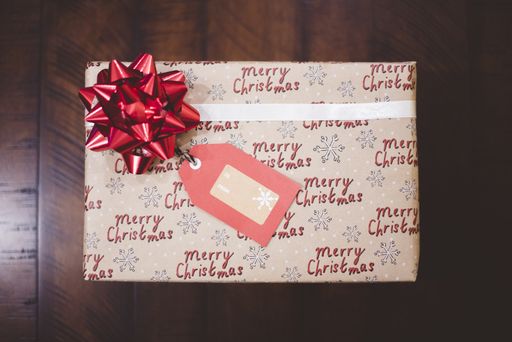 An overhead shot of a present with Christmas wrapping paper on a wooden surface
