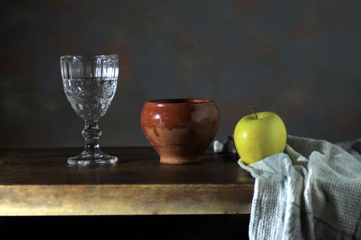 A closeup shot of a bottle, red apples, and a white bowl on the wooden table