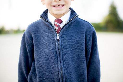 A closeup shot of a boy smiling in a white shirt with a tie under a blue jacket