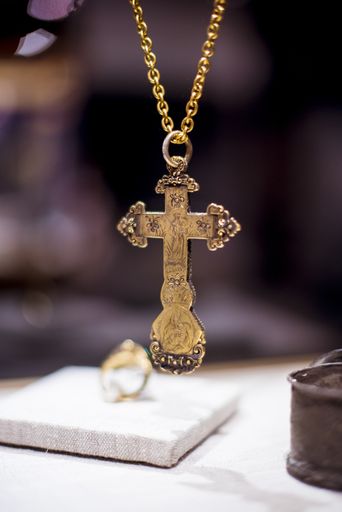 A closeup shot of a big golden Christian cross with depicted icons on a blurred background