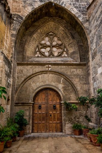 Image of the wood door of an ancient stone church with an arch and a window with beautiful plants in Valencia city, Spain