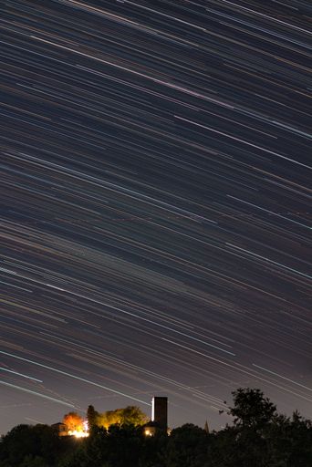 A vertical long exposure shot of the magical starry night sky over the forested hill