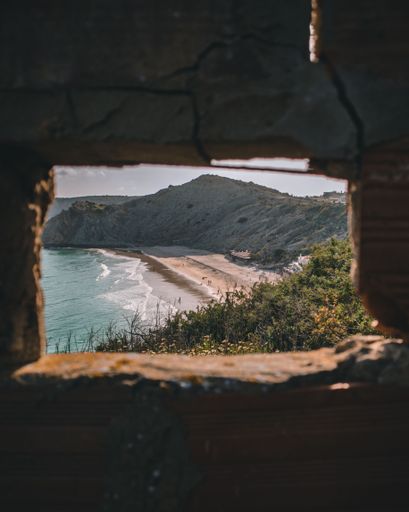 A vertical shot of the beautiful sea shore with the cliff seen through a hole in a stone wall