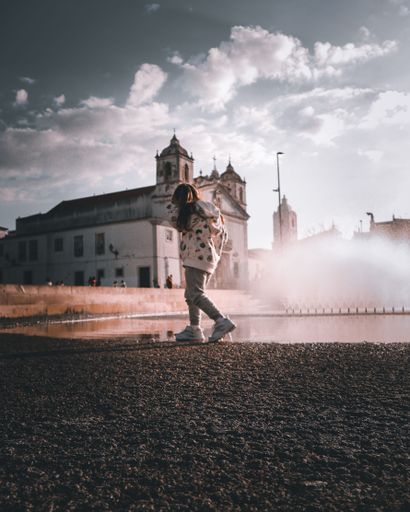 A vertical shot of a girl walking along a river with the church in the background