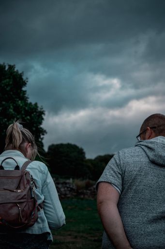 A closeup shot of a man and woman from their back in a natural area under cloudy sky