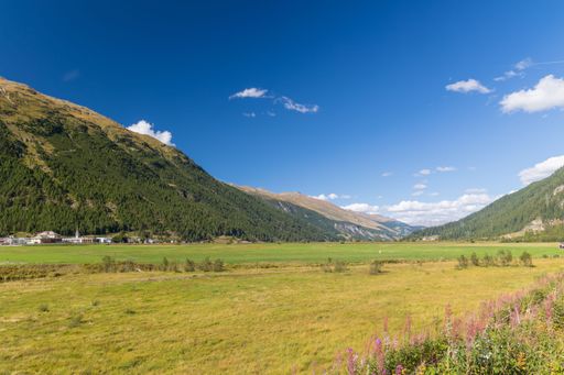 Beautiful landscape over the village in green valley surrounded by high hills, under blue sky with white clouds