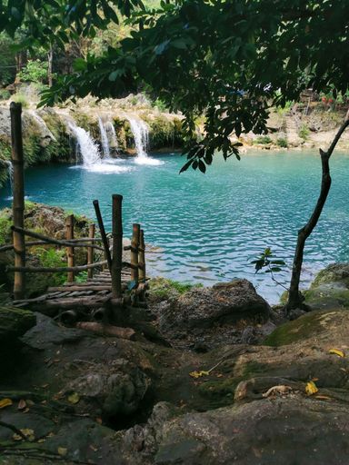 A vertical shot of a small wooden bridge on the shore of a beautiful lake with a waterfall.