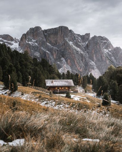 A vertical shot of a cabin on a mountain slope against the rocky Dolomite Alps in Tyrol, Italy