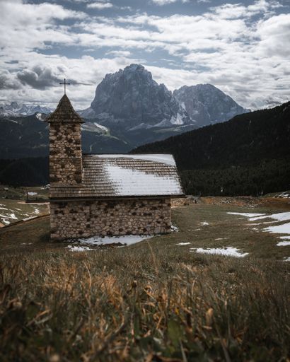 A vertical shot of a small stone church in the Italian Alps on a cloudy day