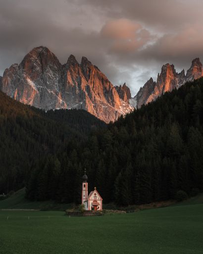 An aerial view of church in background of dense trees and mountains during sunset