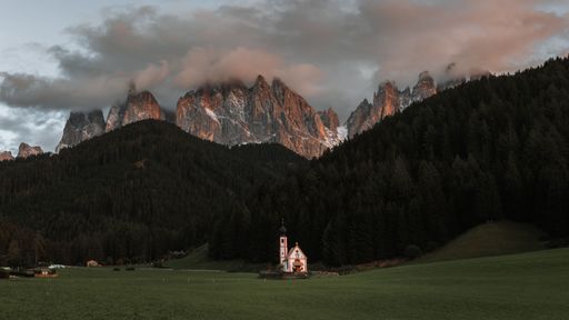 An aerial view of church in background of dense trees and mountains during sunset