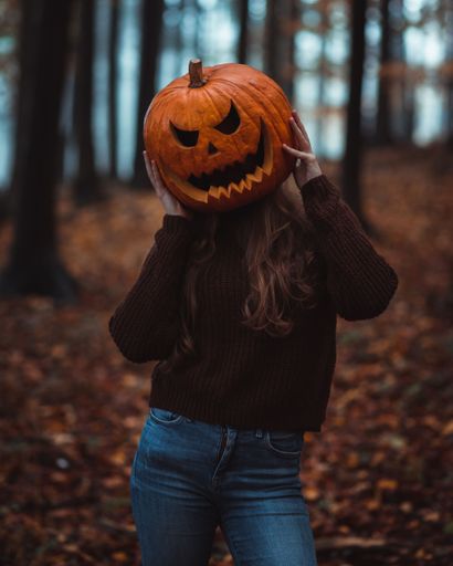 A girl holding a Halloween pumpkin on his head in the forest
