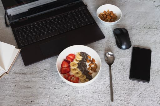 A high angle shot of a bowl of yogurt with fruits and nuts on the table with a laptop on it