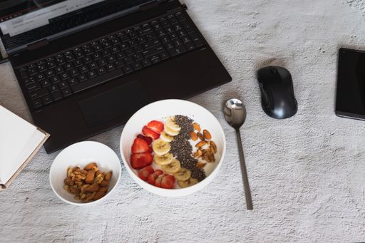 A high angle shot of a bowl of yogurt with fruits and nuts on the table with a laptop on it