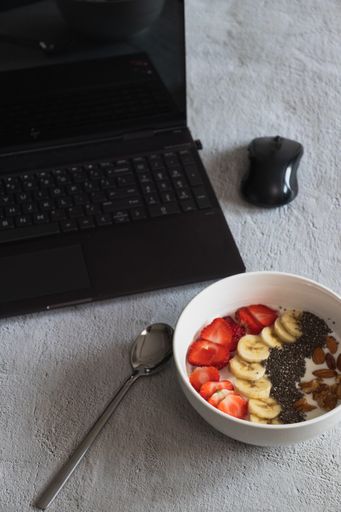 A vertical shot of a bowl of yogurt with fruits and nuts on the table with a laptop on it