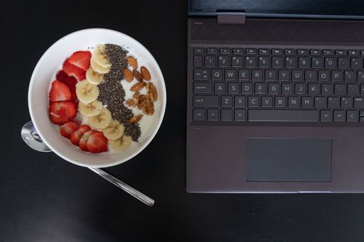 A top view of a bowl of yogurt with fruits on the table with a laptop on it