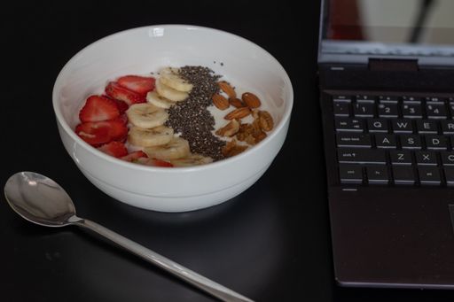 A closeup of a bowl of yogurt with fruits on the table with a laptop on it