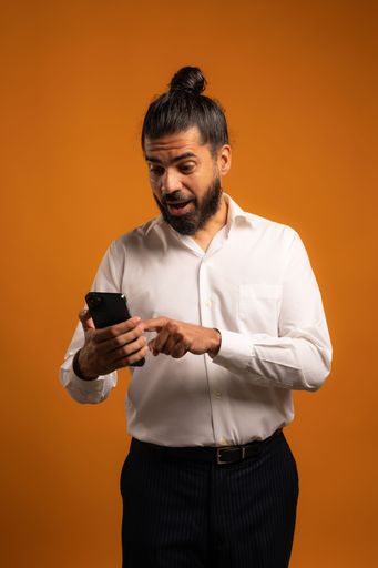 A beautiful shot of a Hispanic man with a phone showing emotions in front of an orange background