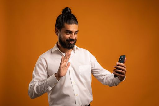 A beautiful shot of a Hispanic man with a phone showing emotions in front of an orange background