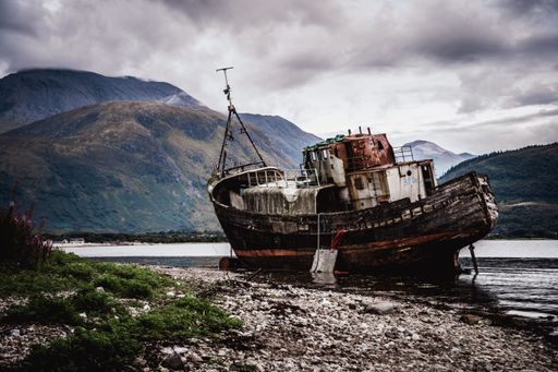 The abandoned Old Boat of Caol in Scotland with mountains under a gloomy gray sky