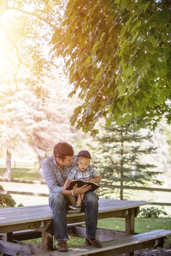 A vertical shot of a male reading the bible for his baby on his lap with a blurred background