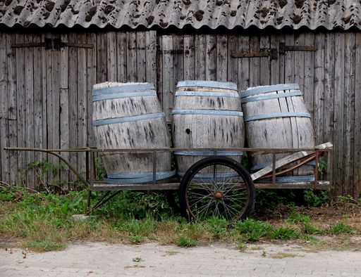 Three old barrels on a wooden cart against the wooden wall of a shed during the daytime