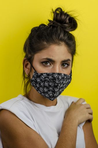 A vertical shot of a Hispanic female with a face mask and thoughtful expression on yellow background