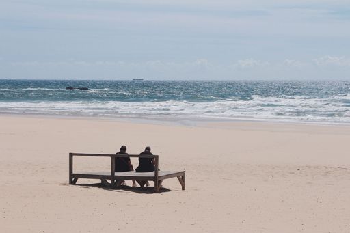 A couple resting on the sandy beach with the foamy sea waves in the background on a sunny day