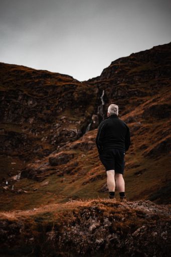A vertical shot of a man standing in front of a hill and looking at it
