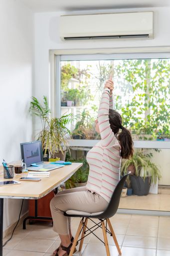 A vertical shot of a young female stretching on a chair while working from home
