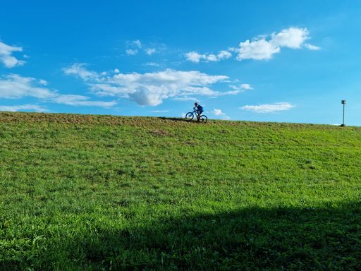 A low angle shot of a person biking up a green hill under a blue sky