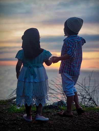 A vertical shot of two kids holding hands on a top of a hill, watching the sunset in Karnataka India