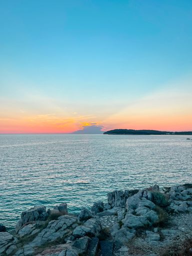A vertical shot of the sunset, rocks in the foreground and the silhouette of mountains on the horizon,Croatia