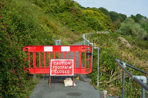 A red barrier and a sign banning the entrance of a narrow road to the forest