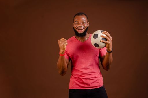 An attractive happy African man holding a soccer ball isolated on a brown background.