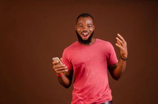 An African man holding his phone and standing in front of a brown background