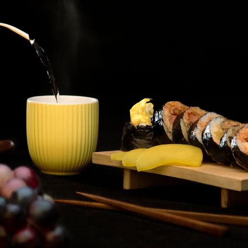 The Korean Gimbap on wooden board and tea pouring into yellow cup on dinner table
