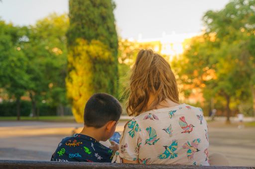 A back view of a female showing content on her mobile phone to her son in the park