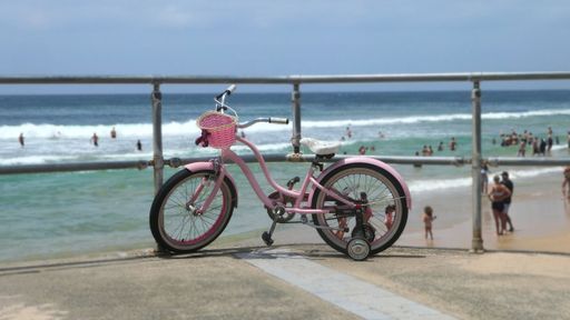 A little pink bike parked against a railing at a beach in Sydney, Australia