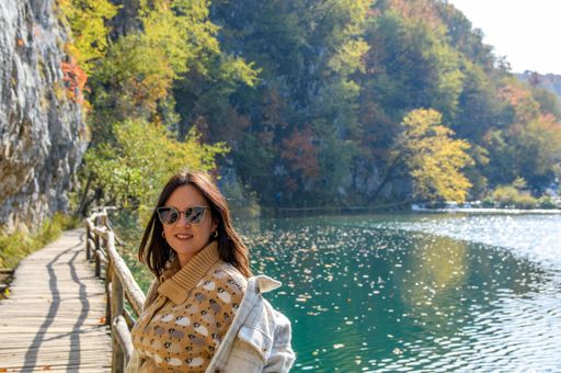 A closeup shot of a white smiling female before a glowing lake at Plitvice Lakes national park