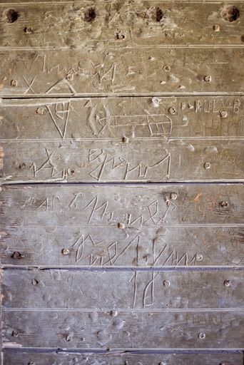 A vertical shot of engravings on wall made of wooden desks
