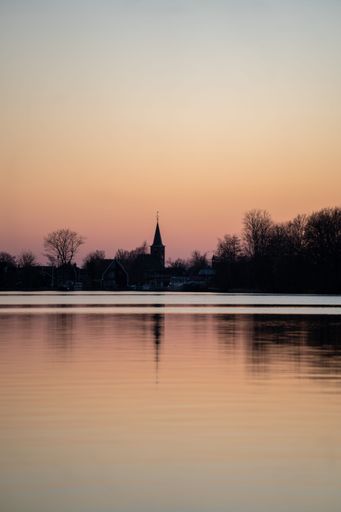 Vertical shot of a lake with reflection of a village at sunset