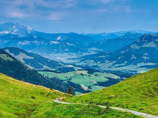 A scenic shot of a trail road in the middle of a field overlooking mountain valleys