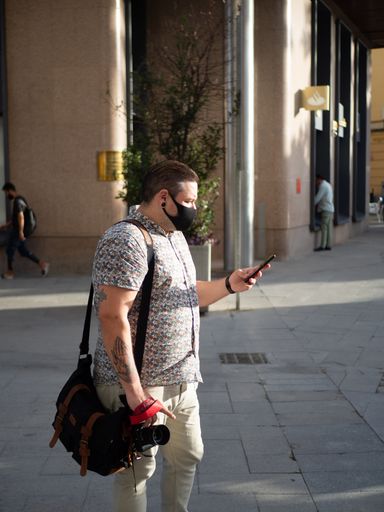 A vertical shot of a male wearing a medical mask and using his phone outdoors